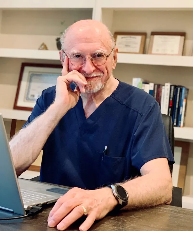 Dr. Joseph Feste, seated in his office, in navy scrubs, smiling warmly